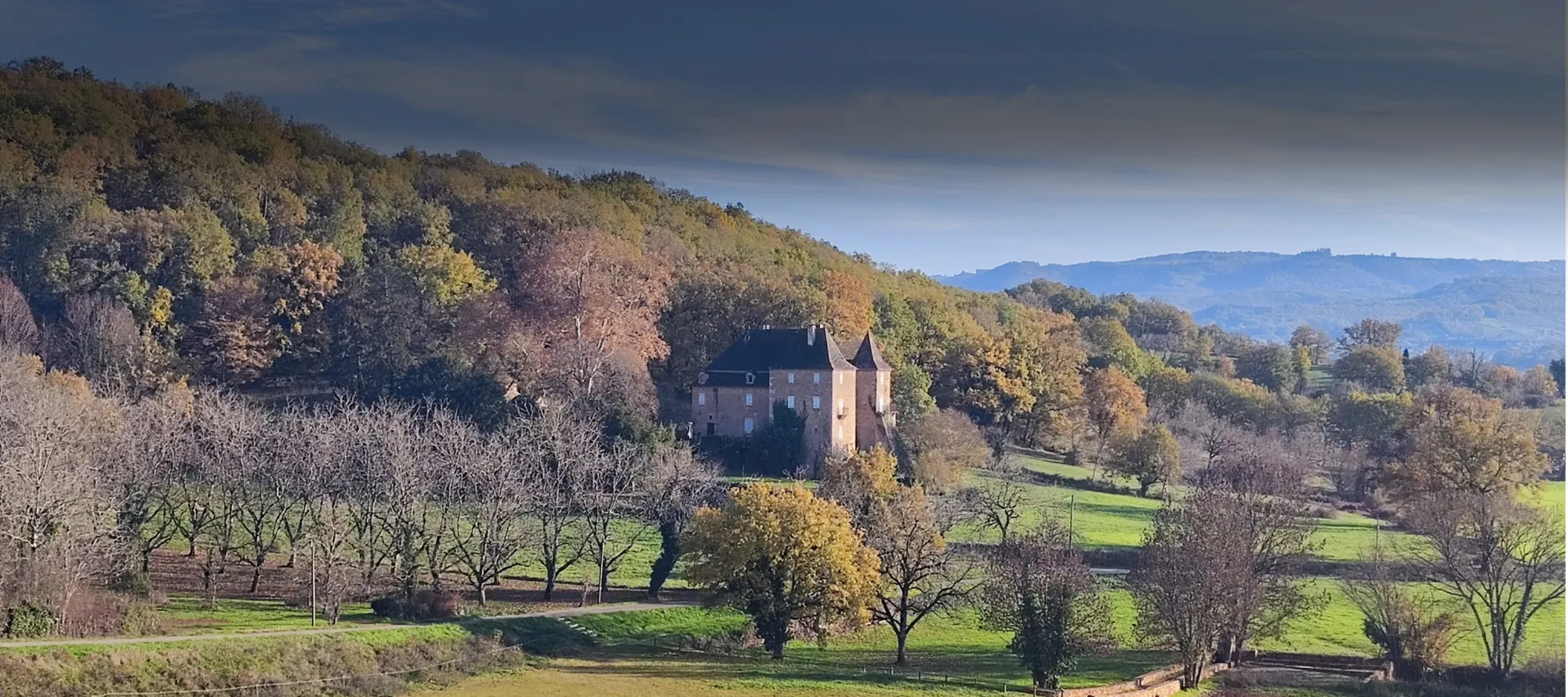 Château du Boscau van bovenaf gezien in de vallei, omringd door bos in herfstkleuren en weilanden
