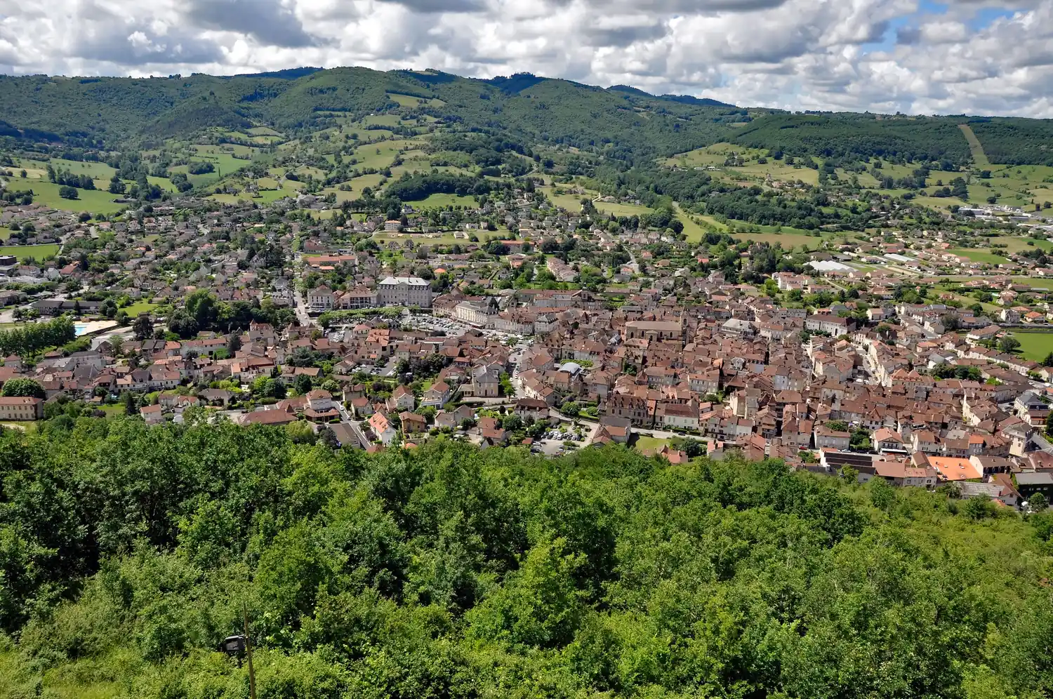 Saint-Céré seen from the hillside, with the town's red roofs in the valley between the hills of the Ségala